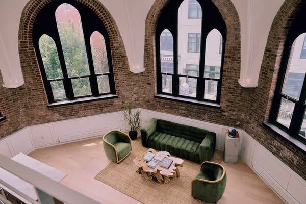 A living room with a green couch, two green chairs and a live edge coffee table set near three sets of windows.
