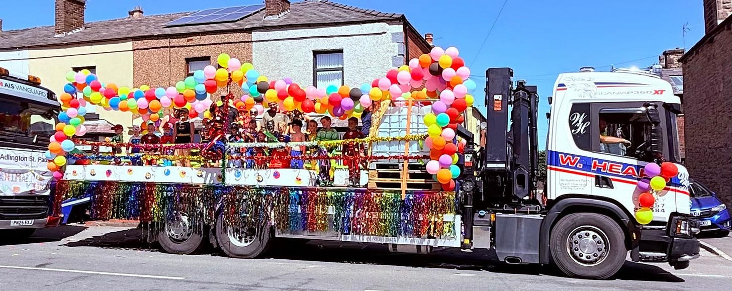 A long white truck with people stood on the back surrounded by multicoloured balloons and ribbons.