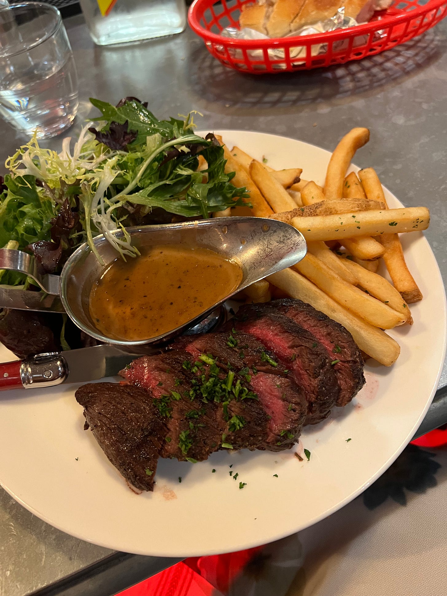 A sliced hanger steak with peppercorn sauce, served with french fries and a mixed greens salad at Bouillon by Moulin.