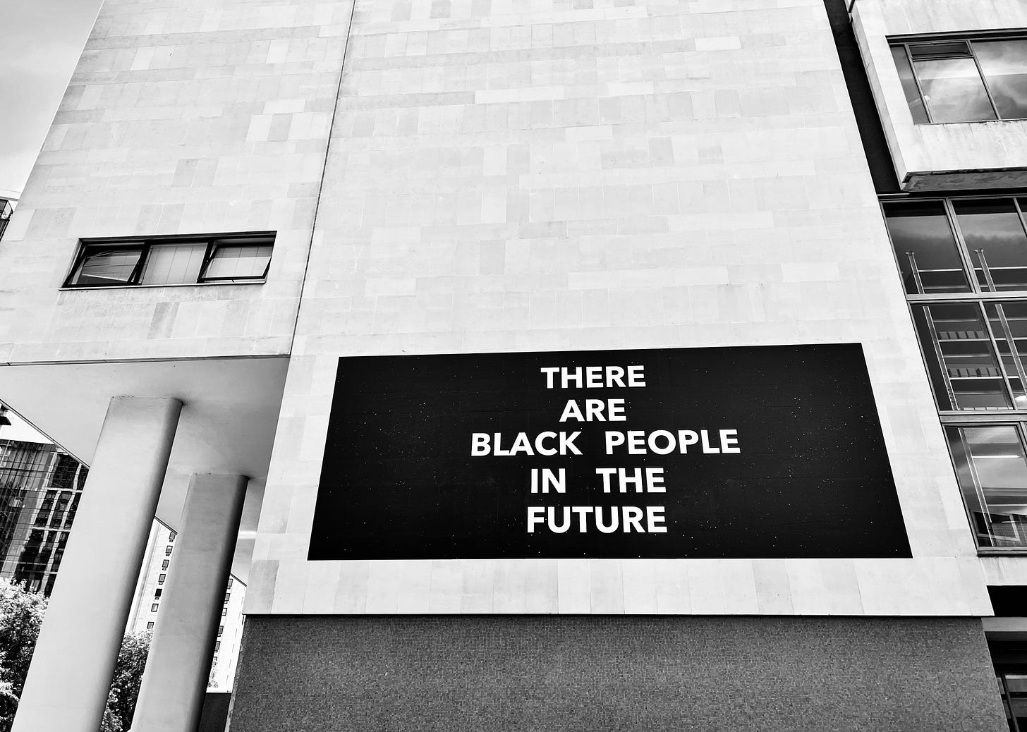 Black and white photo of a solid black rectangular text artwork by Alisha B. Wormsley on the side of the Royal Festival Hall in London’s South Bank. The artwork is a plain black rectangle with white text in large capitals “THERE ARE BLACK PEOPLE IN THE FUTURE”. Black and white photo of a solid black rectangular text artwork by Alisha B. Wormsley on the side of the Royal Festival Hall in London’s South Bank. The artwork is a plain black rectangle with white text in large capitals “THERE ARE BLACK PEOPLE IN THE FUTURE”.
