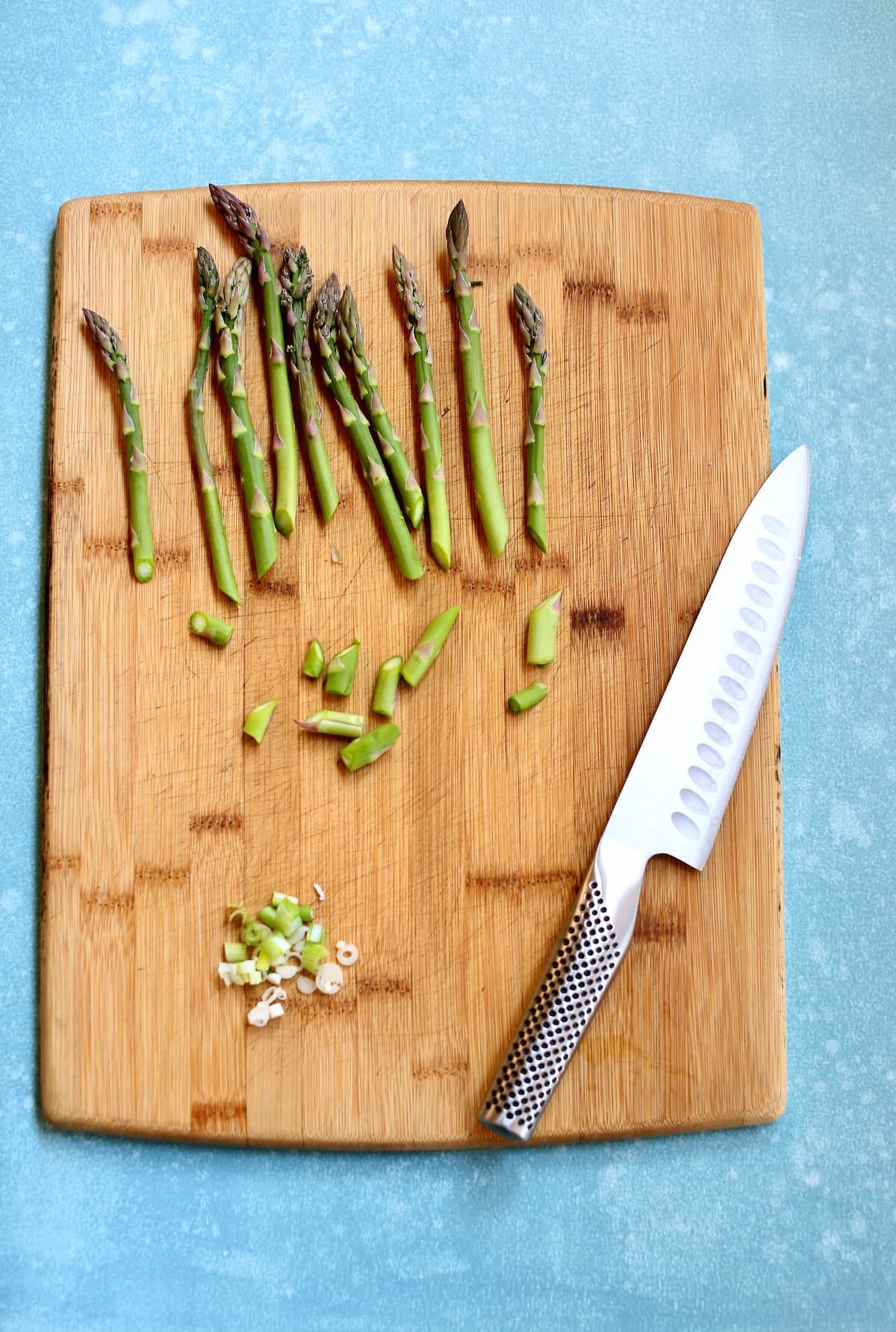 a cutting board with a knife and asparagus spears being trimmed.
