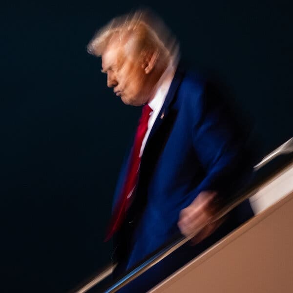 President Trump walking down the steps of Air Force One at night. A slow shutter speed has made the image slightly blurry. 