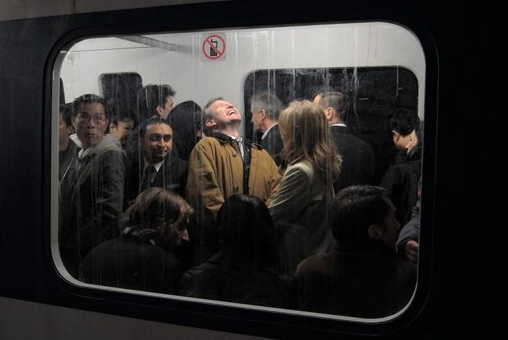 This may contain: a group of people standing next to each other on a subway train, looking out the window