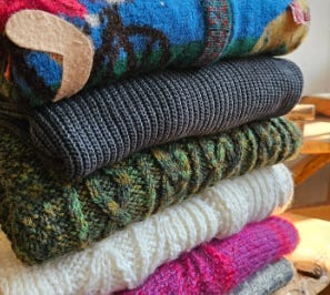 stack of vintage sweaters, boxes filled with Christmas ornaments, flat lay of vintage jeans and cowboy boots.