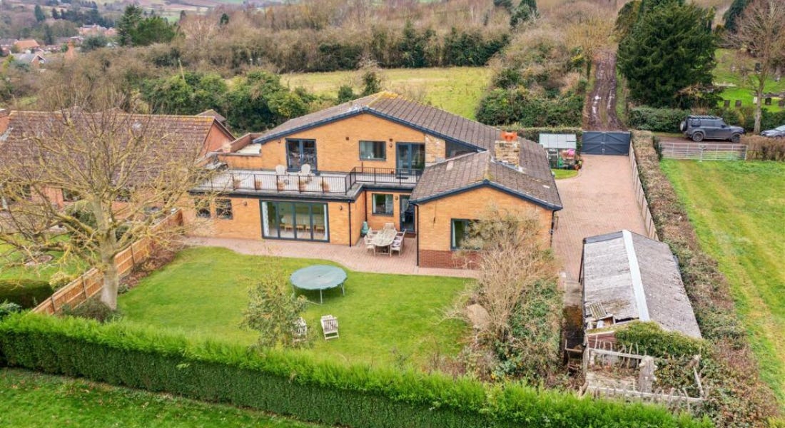 A brick house with a balcony, a large garden, and the countryside around it