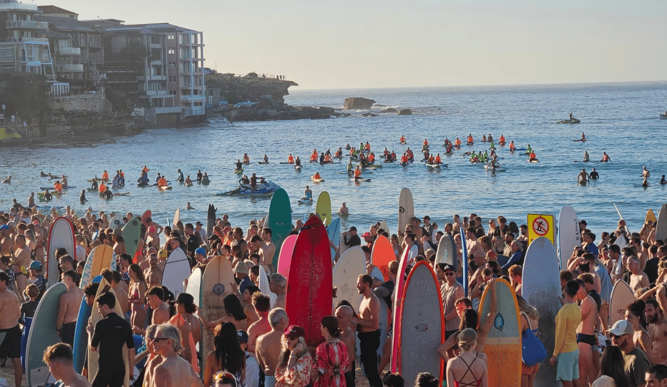 Crowded Bondi Beach with surfers holding colourful surfboards on the sand and in the water in the early morning. Crowded Bondi Beach with surfers holding colourful surfboards on the sand and in the water in the early morning.