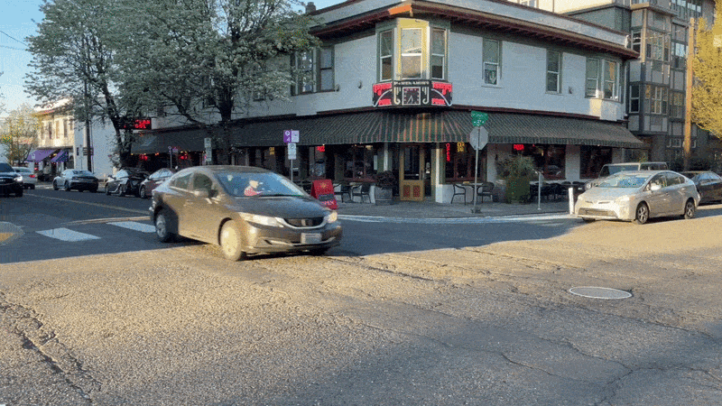 Cars drive across an intersection that has cracked pavement and deep wheel ruts in Portland's Northwest 23rd neighborhood.
