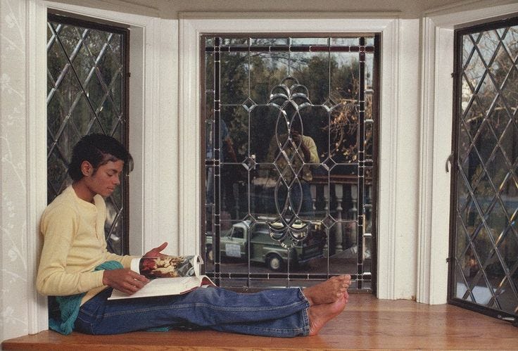 This may contain: a young man sitting on the floor reading a book in front of a glass door