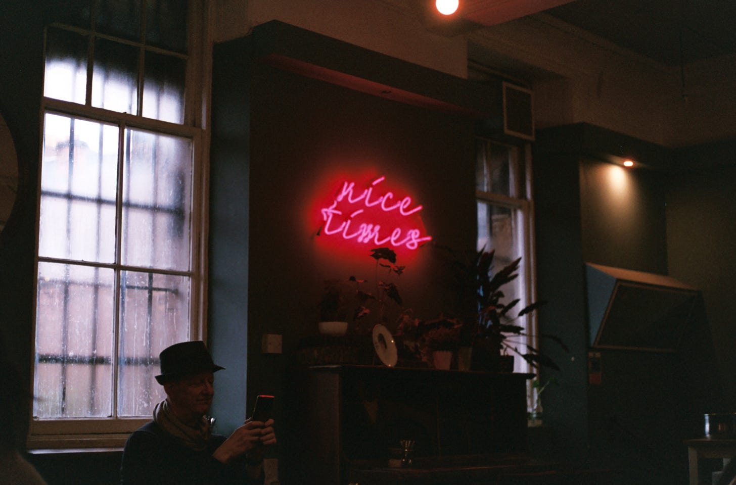 A dark film photo of Lovecrumbs café in Edinburgh, focusing on a pink neon sign on the wall that reads 'nice times'.