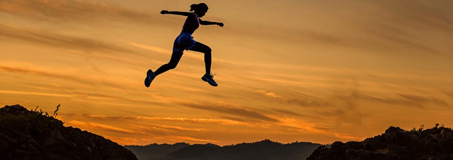 A young athletic woman leaps across a trench and is suspended in midair at sunset.