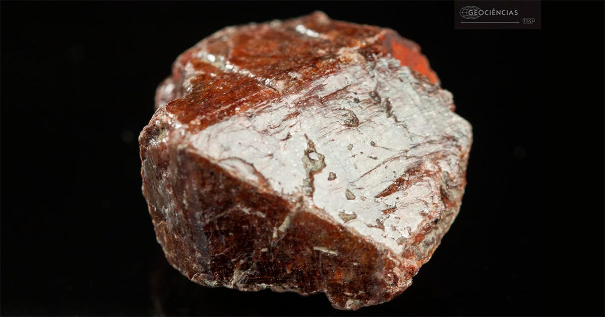 Imagem macroscópica de um cristal de zircão de tom castanho-avermelhado captada em contraste com um fundo preto. Imagem macroscópica de um cristal de zircão de tom castanho-avermelhado captada em contraste com um fundo preto.