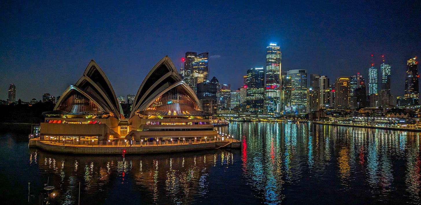 The Opera House glittering at night, downtown Sydney behind it. 