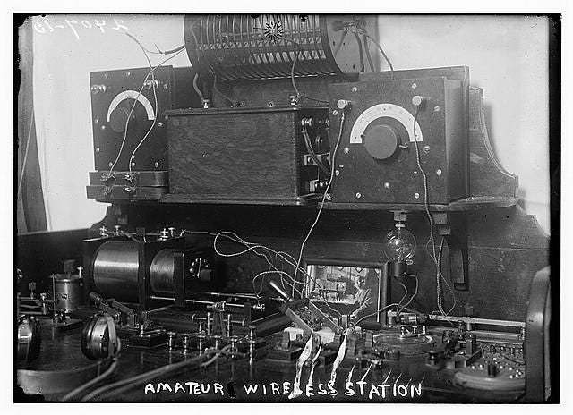 a black and white photo of a large box with several wires, knobs, and headphones. The photo is captioned 'amateur wireless station' a black and white photo of a large box with several wires, knobs, and headphones. The photo is captioned 'amateur wireless station'