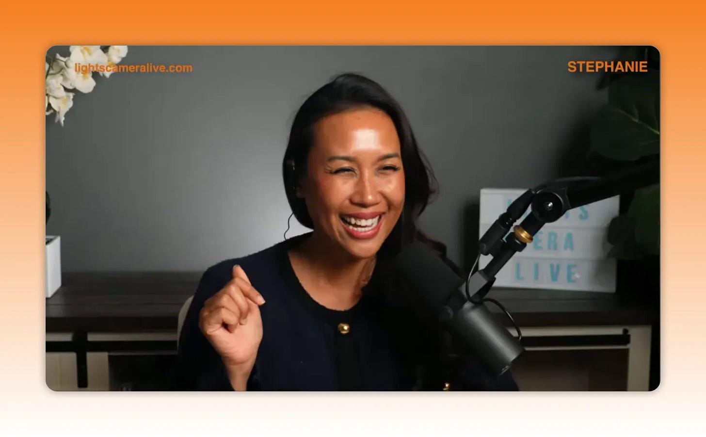 Host smiling and speaking into a broadcast microphone, demonstrating confident on-camera energy