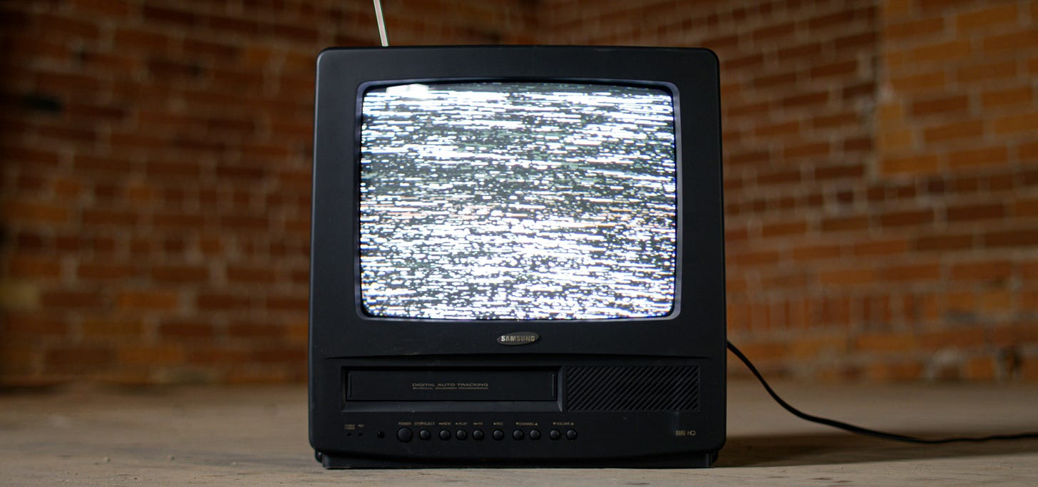 90s era TV monitor with built-in VCR showing glitchy static snow, set in an abandoned industrial room, illustrating themes of trash cinema and analog decay.
