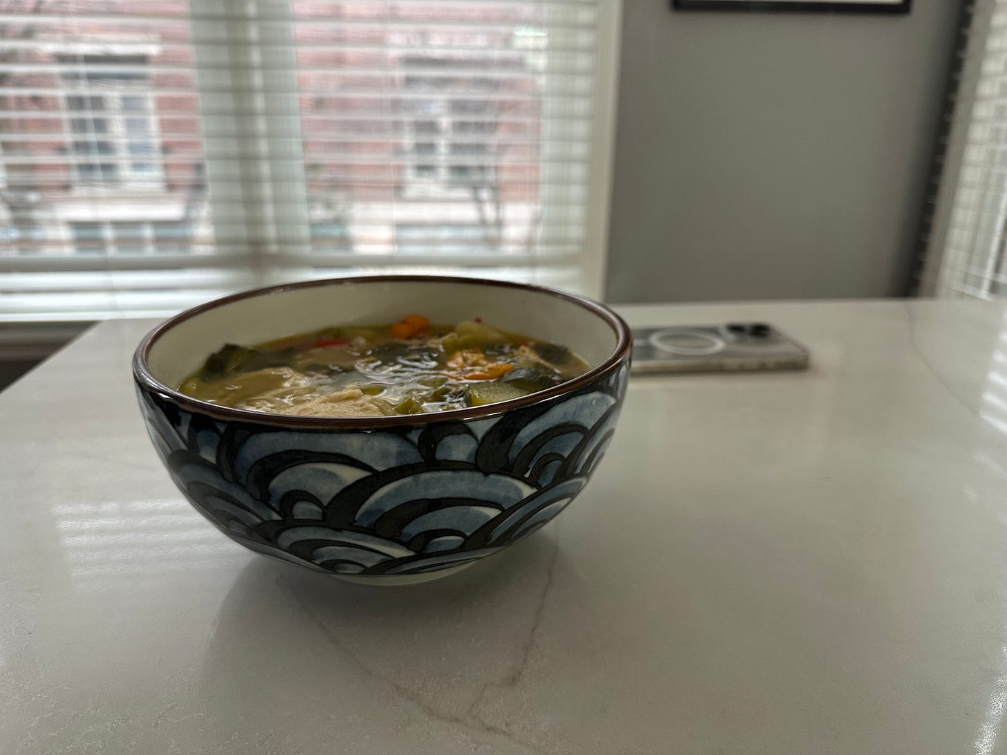 A warm bowl of soup on a white kitchen counter, phone face-down in the background.