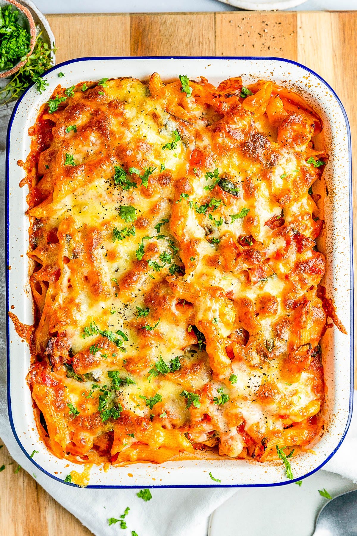 Baked pasta dish with melted cheese and parsley served in a white rectangular dish on a wooden surface. Baked pasta dish with melted cheese and parsley served in a white rectangular dish on a wooden surface.