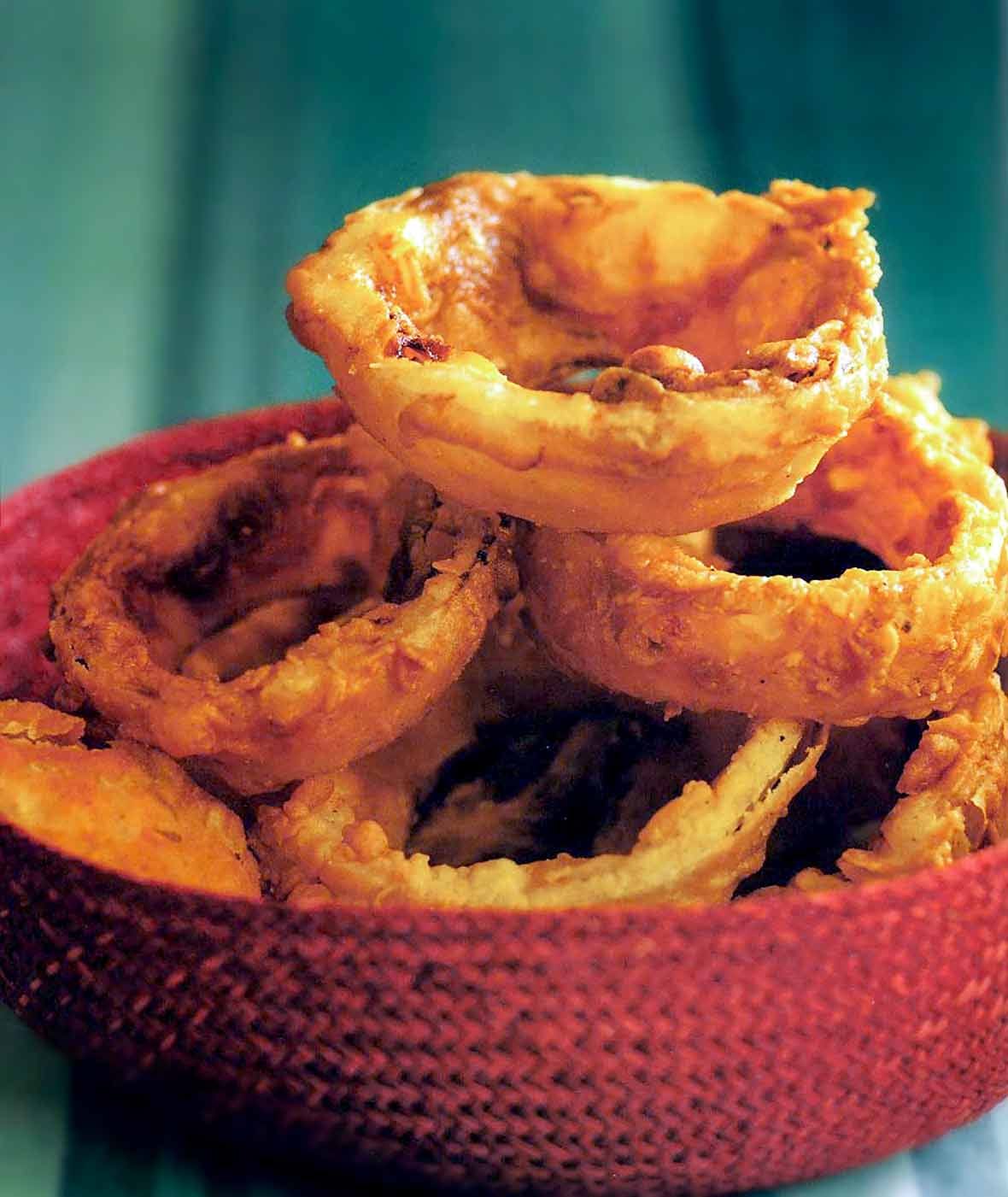 A red basket filled with extra crispy, golden-brown buttermilk fried onion rings.