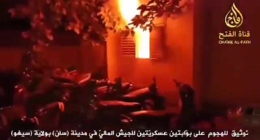 A nighttime scene of a building engulfed in orange flames with black smoke billowing upward, surrounded by trees and structures, Arabic text overlay reading صاروخية على مخفر الدرك والشرطة المالية بمنطقة سان and a logo labeled CHAINE AL FATIH.