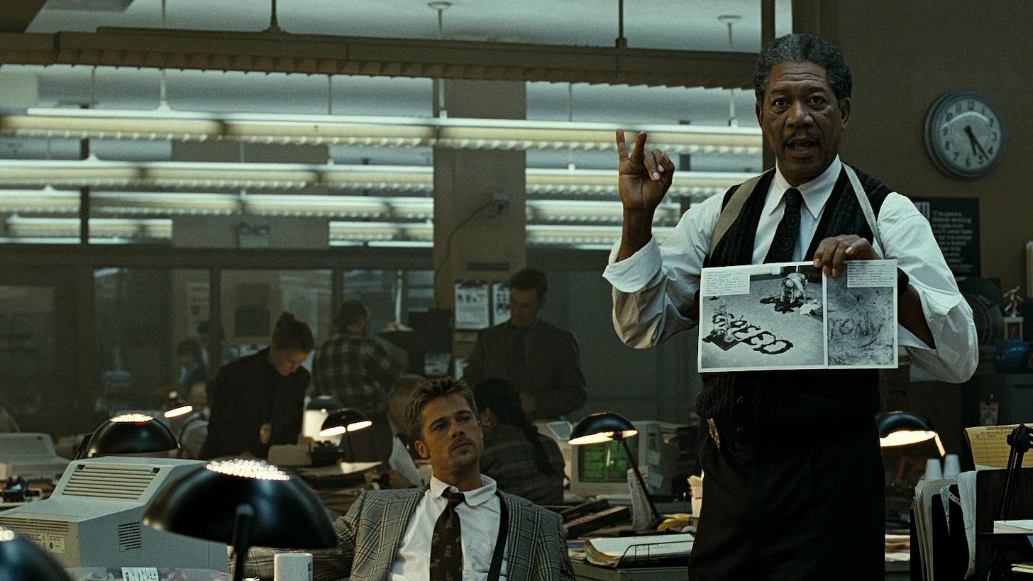 Se7en | Still features Brad Pitt as Detective Mills observing Morgan Freeman's Detective Somerset holding a picture that reads "GREED."