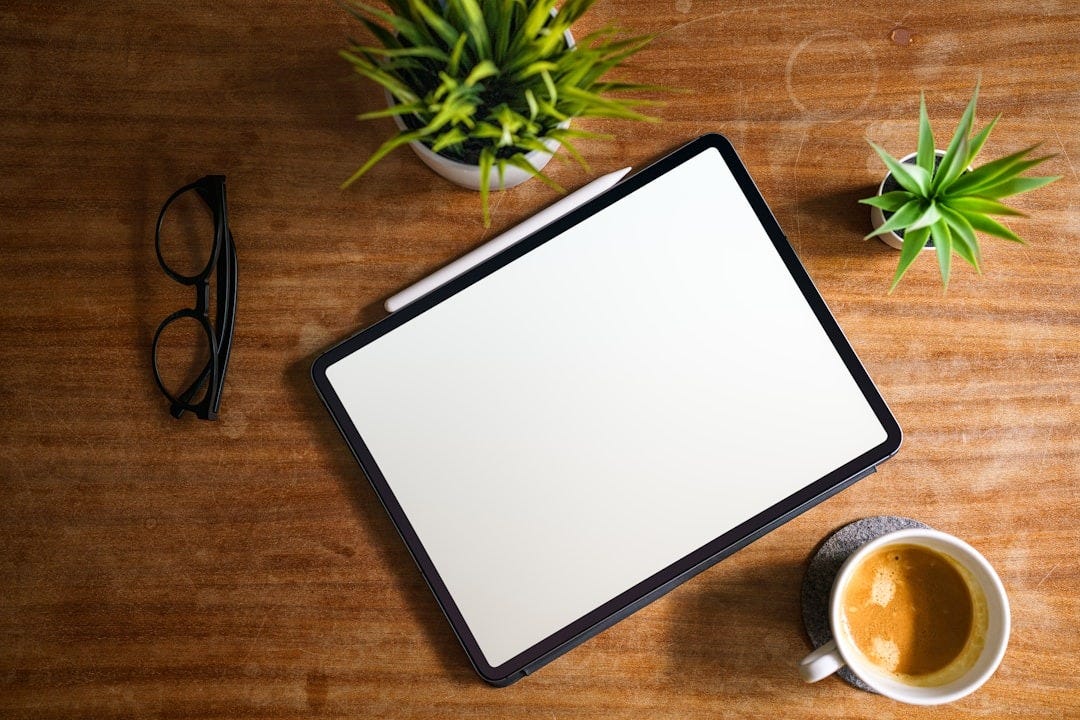 A tablet computer sitting on top of a wooden table next to a cup of coffee