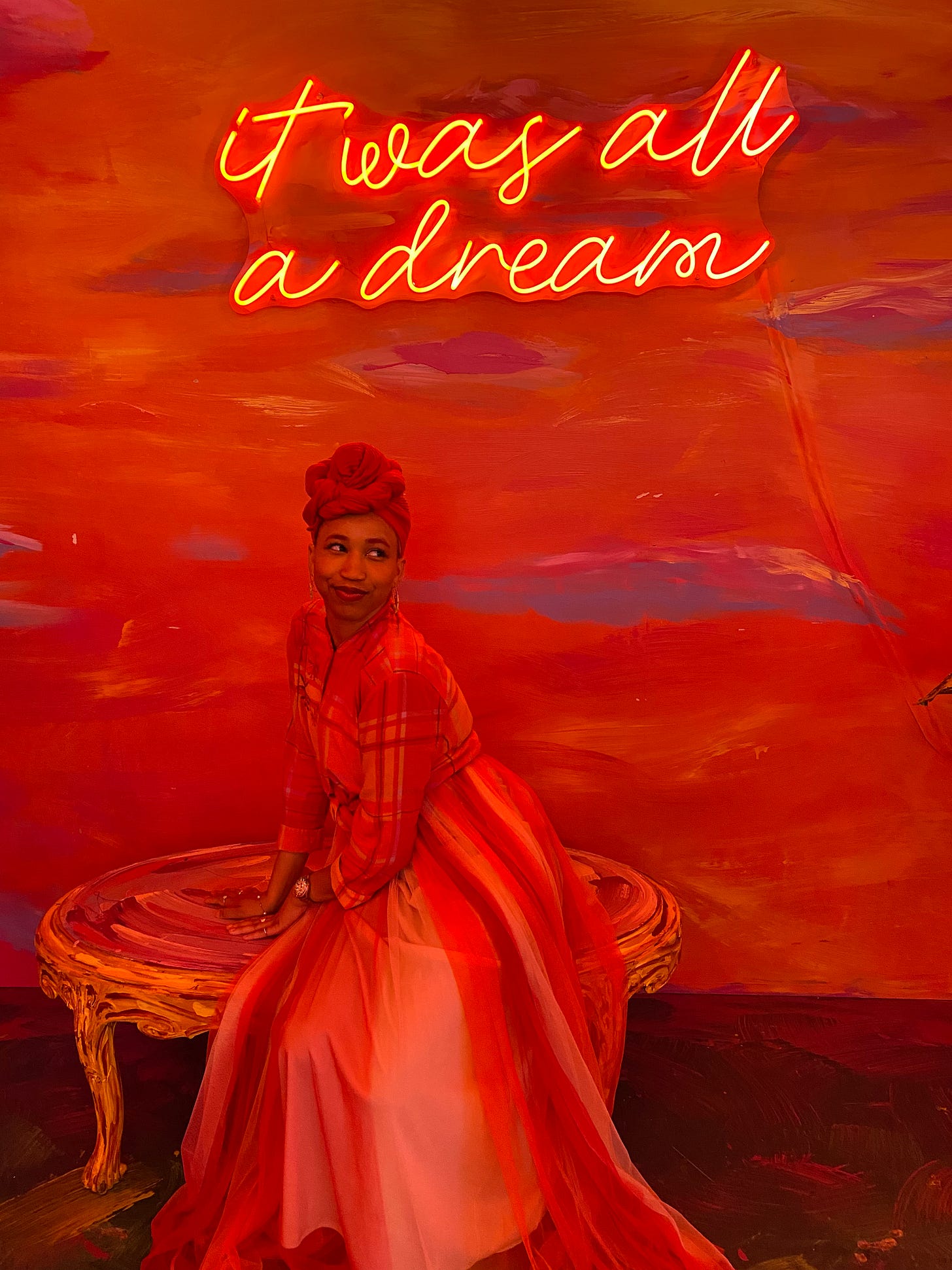 Kiana at the Wonderland Dreams exhibit. A neon sign hanging above her head says It was all a dream