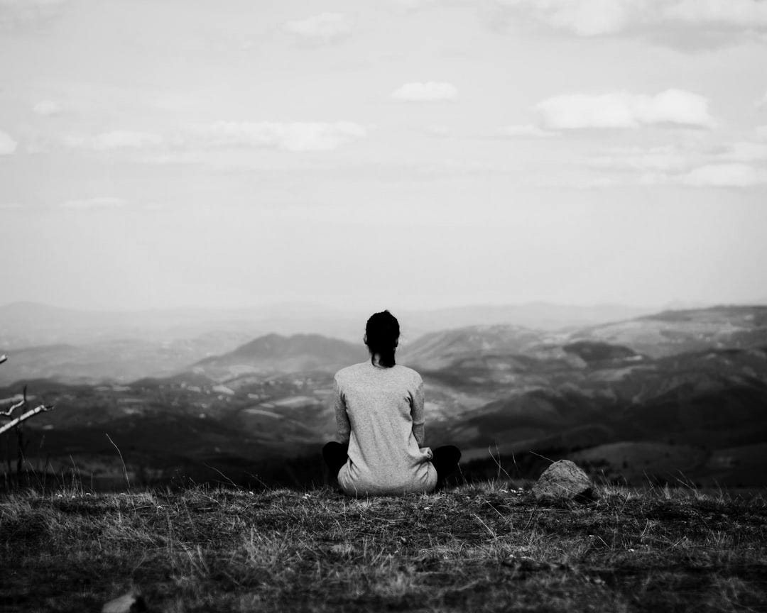 woman sitting on cliff overlooking mountains during daytime woman sitting on cliff overlooking mountains during daytime