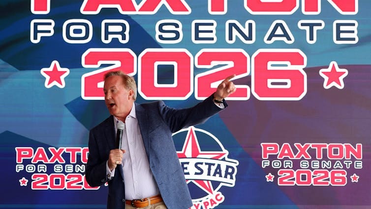 Middle-aged man wearing a suit jacket gestures and speaks into a microphone in front of a massive banner reading 'Paxton for Senate 2026.' Middle-aged man wearing a suit jacket gestures and speaks into a microphone in front of a massive banner reading 'Paxton for Senate 2026.'