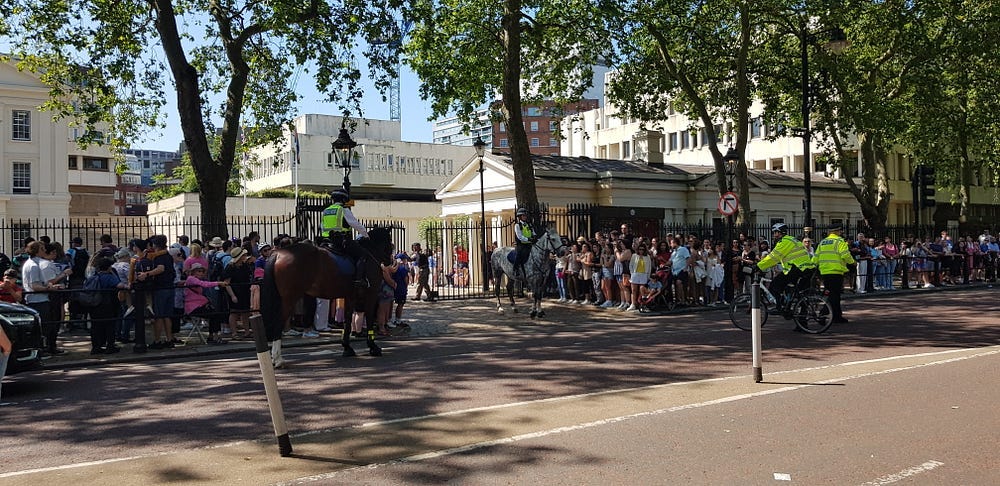 Mounted Police assisting with crowd control on either side of the gates to Wellington Barracks and two other police officers wearing high-viz jackets.
