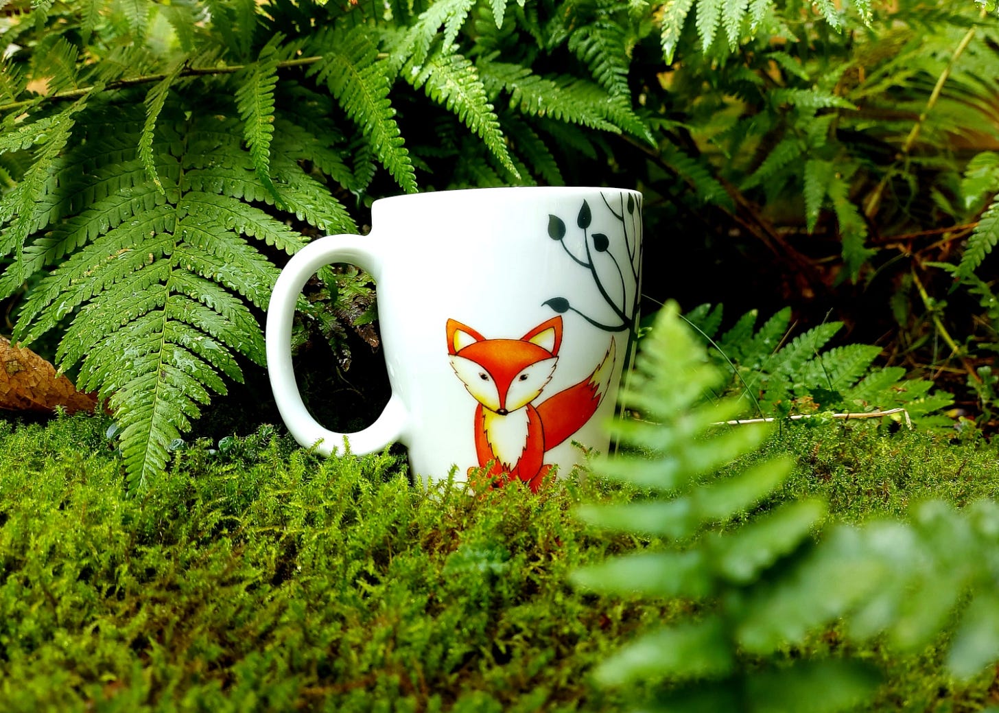 Fox mug on moss surrounded by fern