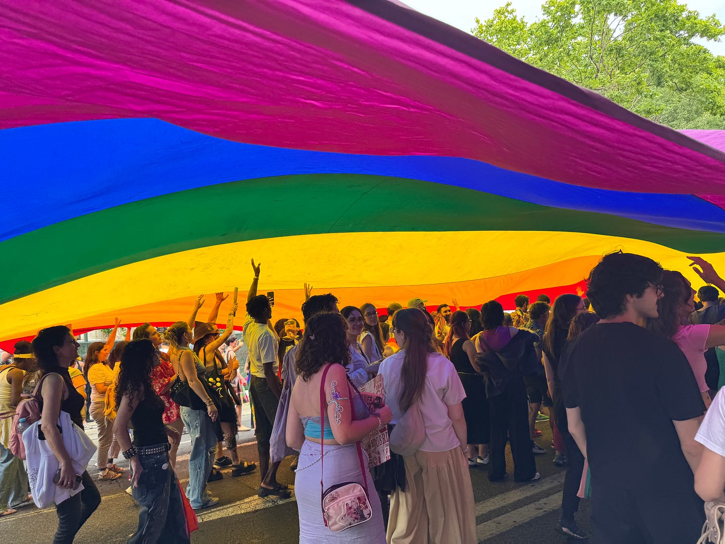 Young people walk beneath a giant rainbow flag. Young people walk beneath a giant rainbow flag.