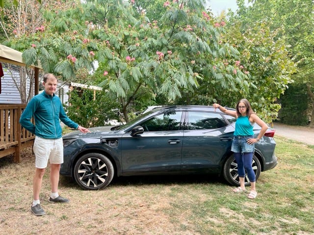 Two people standing next to a hybrid car, looking sad