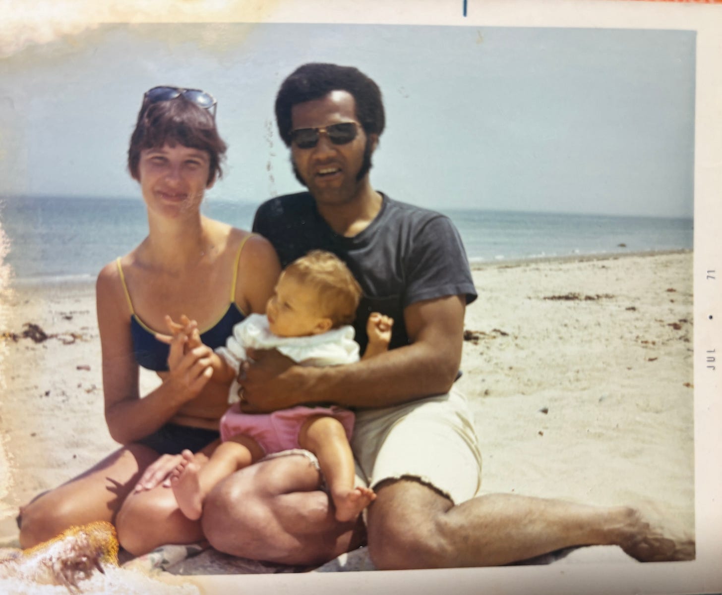 lithuanian american woman and african american man, married couple sitting together holding their one year old child on their laps at the beach manomet massachusettes 1971