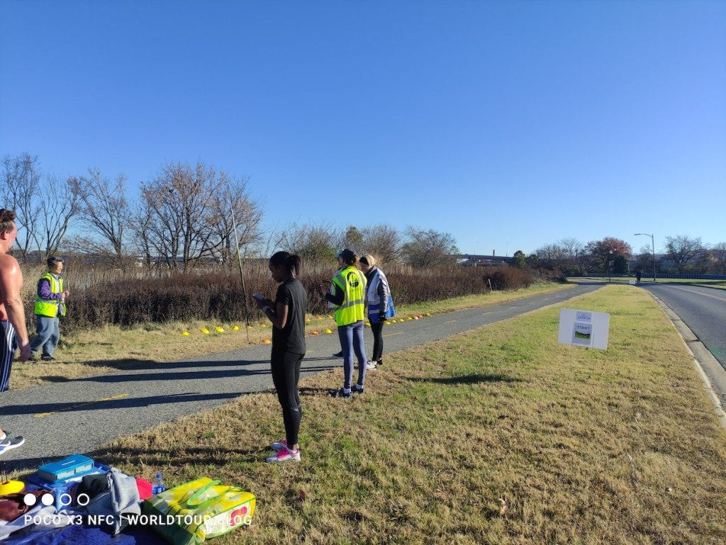 The finish line, next to waist-high scrub bushes with some spindly trees behind, by the river