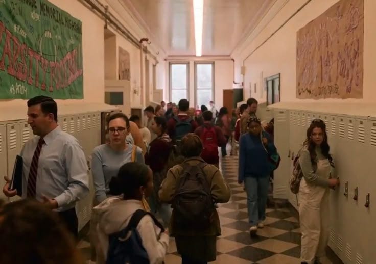 This may contain: a group of people standing in a hallway next to lockers with posters on the walls