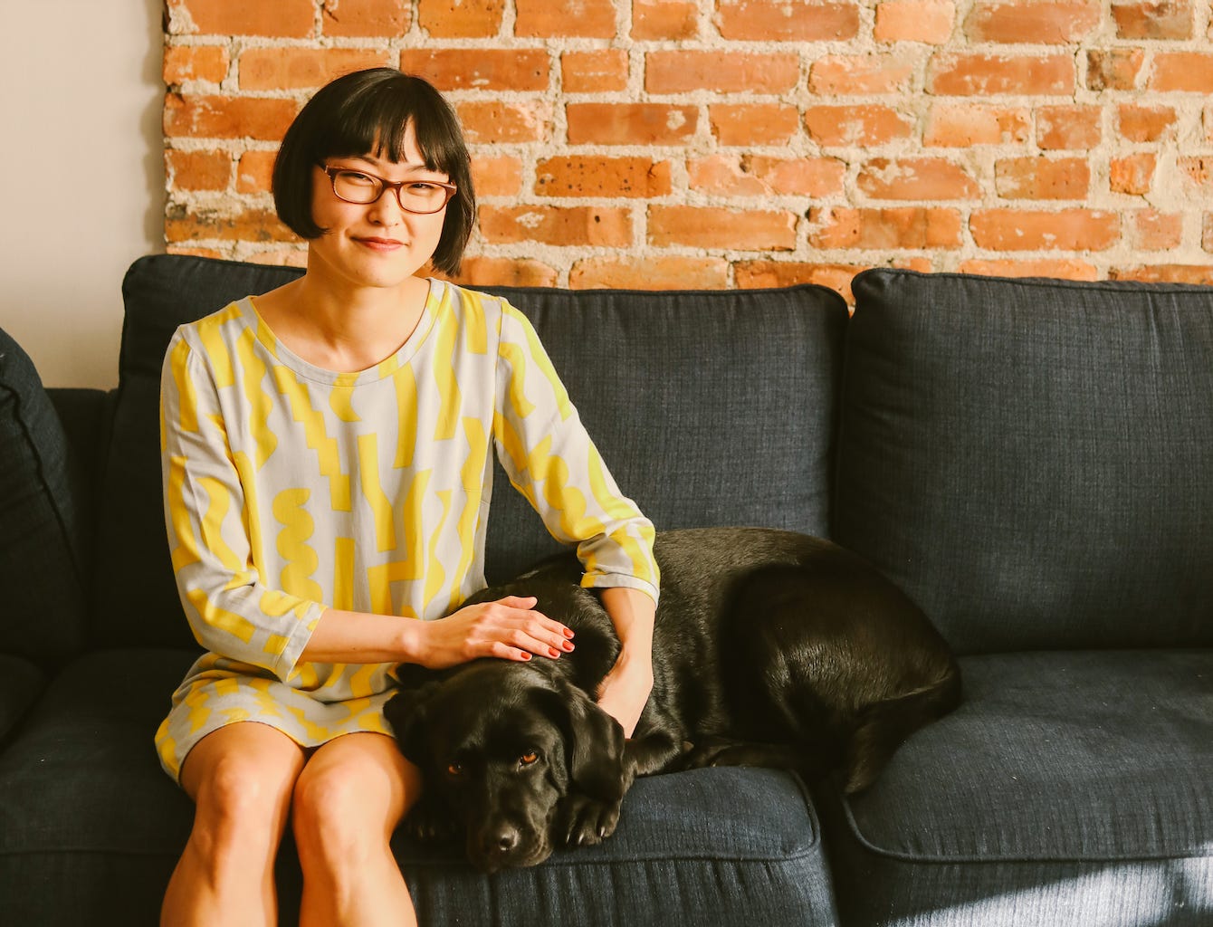 Hannah on a dark sofa with her black lab.