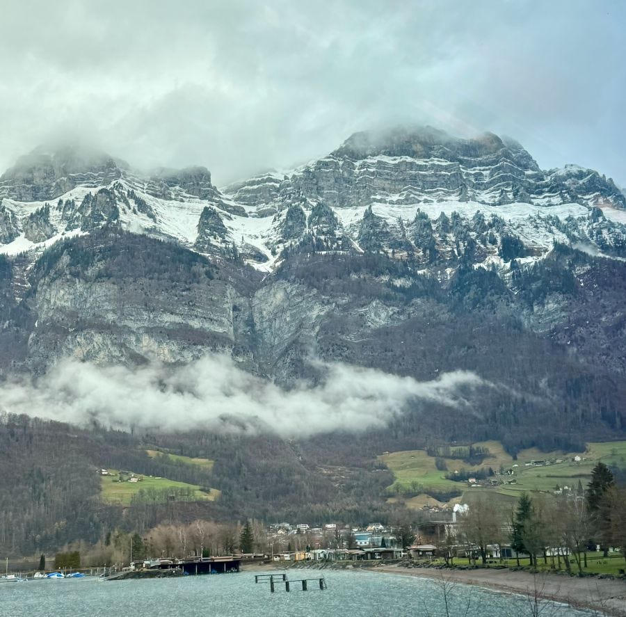 Water, houses and Swiss alps with snow on the craggy granite mountains