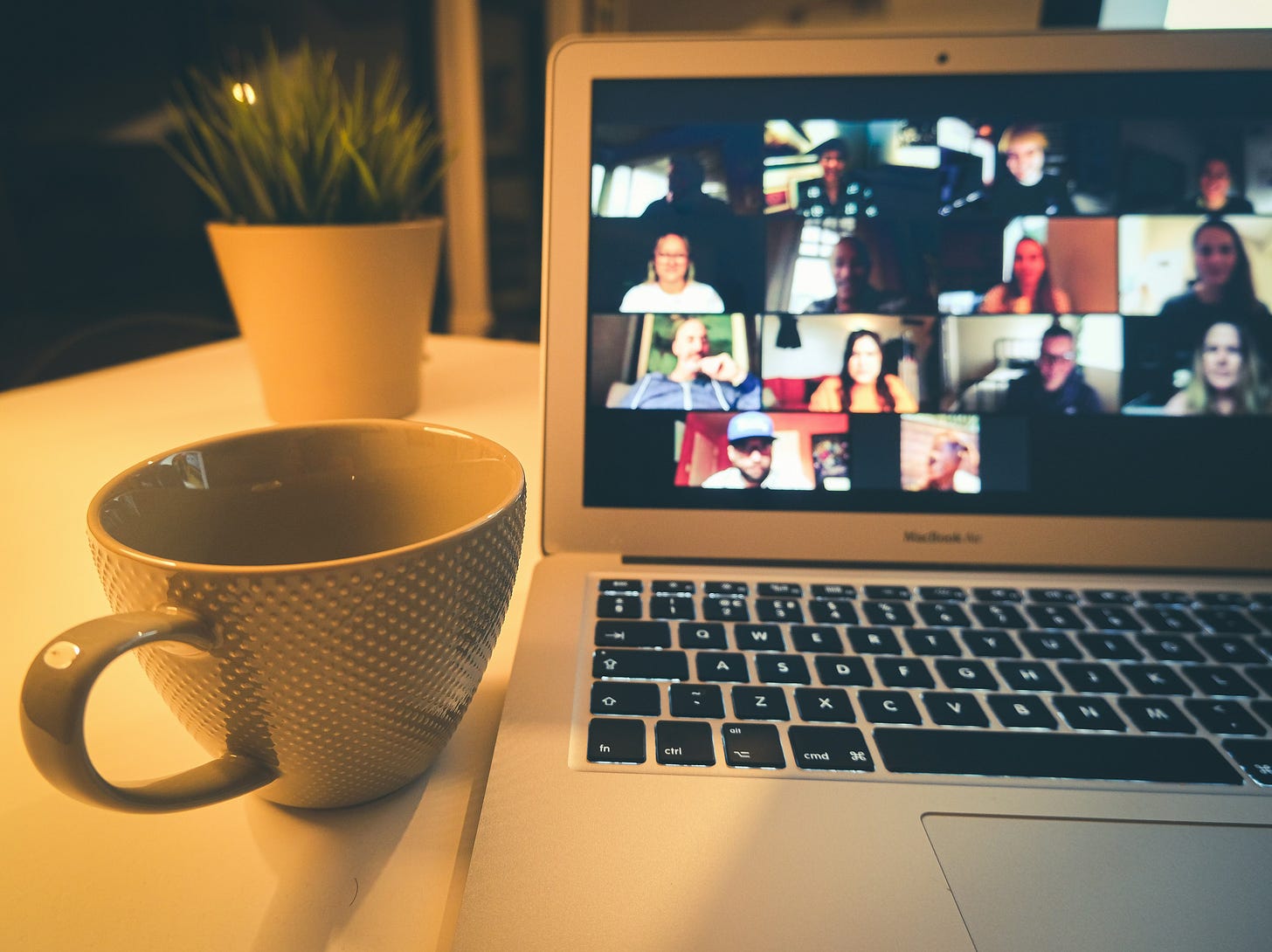 laptop with zoom meeting attendees on display a cup and a plant in the background