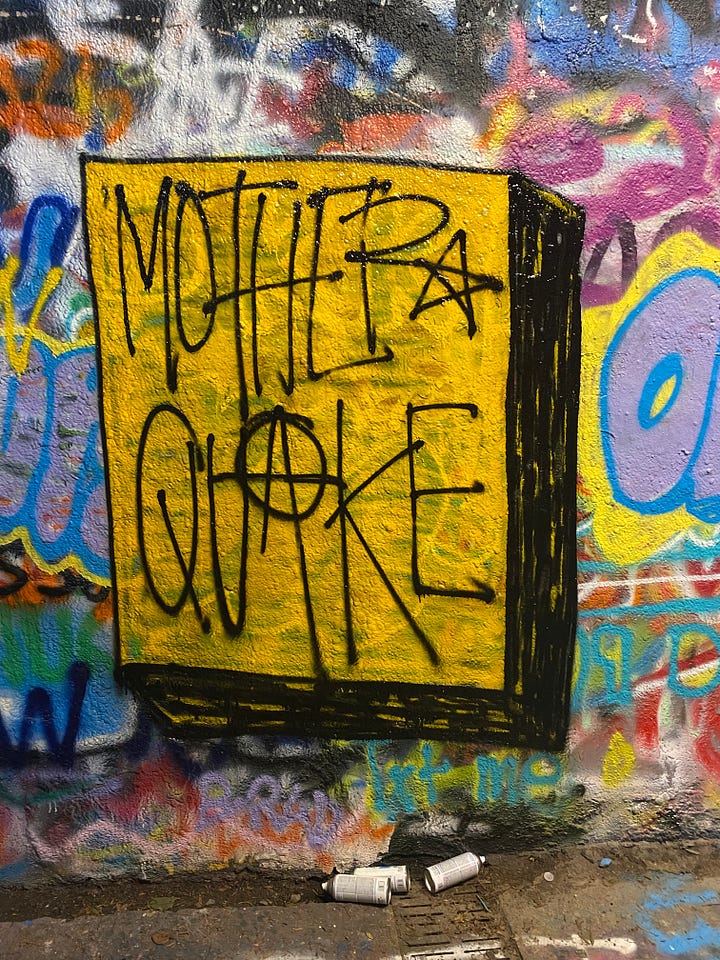 Black, white, and pink "DOWN" on a graffiti wall, over 100 handwritten "aesthetic" stickers on a rolling chair, "Like" painted in blue, yellow, and white facing up and down, and "motherquake" painted in black on a yellow square.