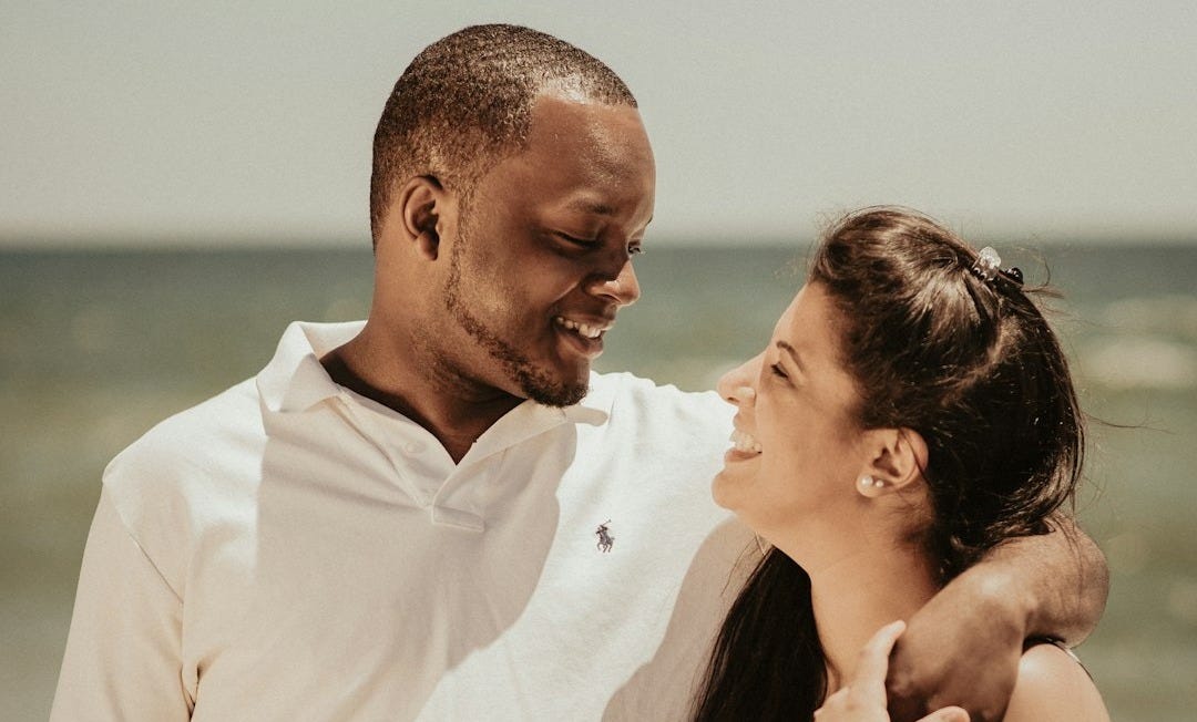man in white polo shirt kissing woman in black and pink floral dress