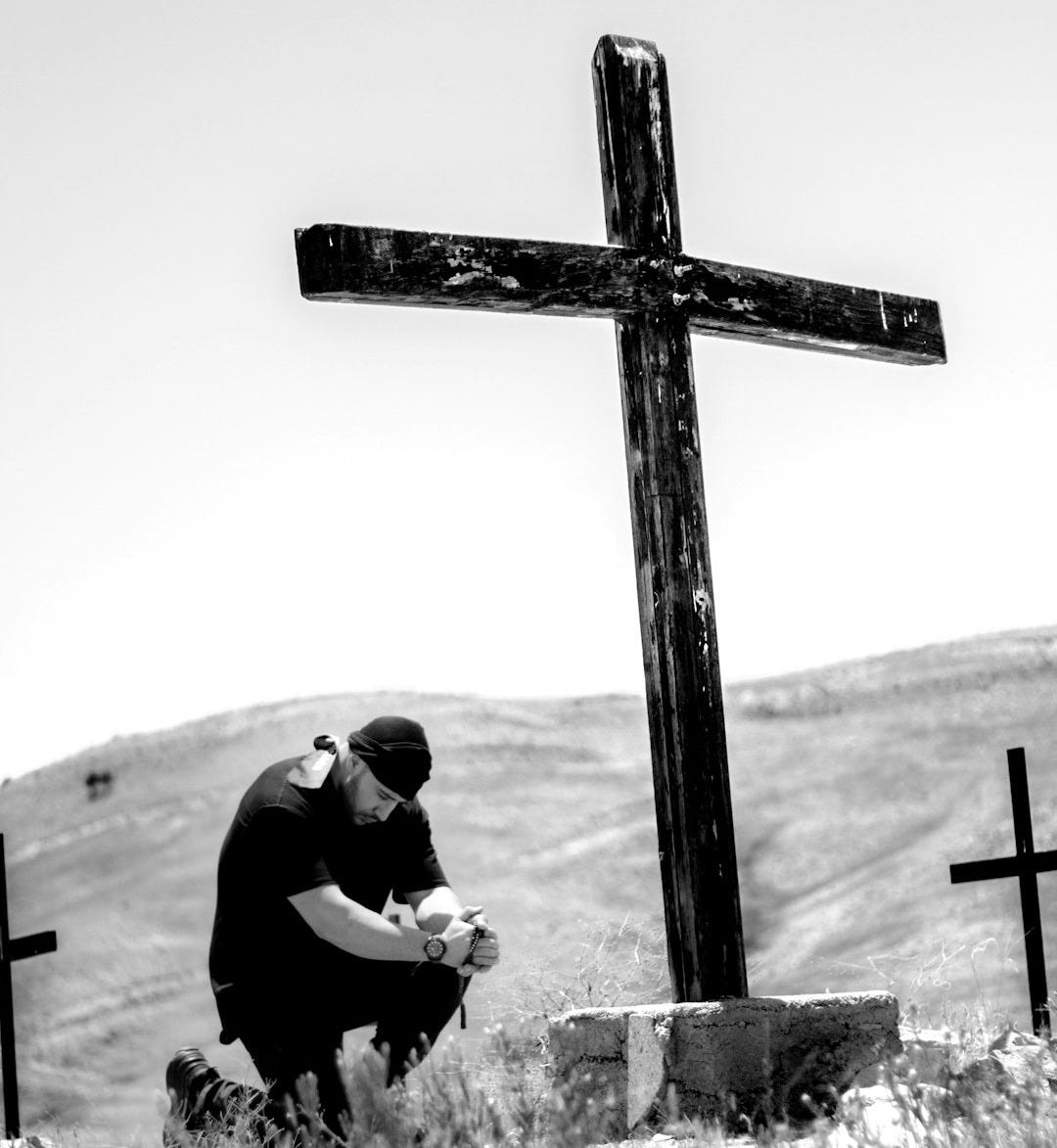 man kneeling in front of wooden cross