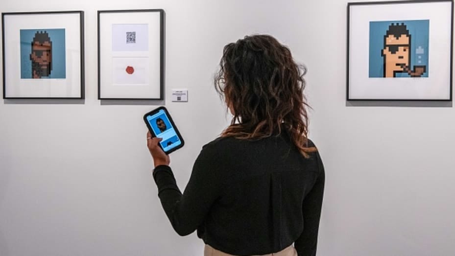 A gallery assistant holds up a smartphone displaying the gallery's online marketplace near an NFT and signed lithograph "Sealed Cryptopunk #3036" by Larva Labs. Photographer: Chris J. Ratcliffe/Bloomberg via Getty Images