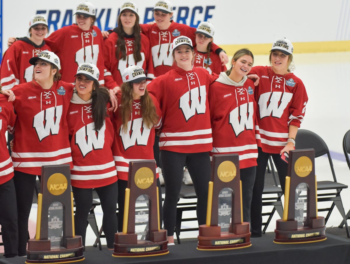 Four national championship trophies sit on a table while a row of players stand with linked arms in front of them