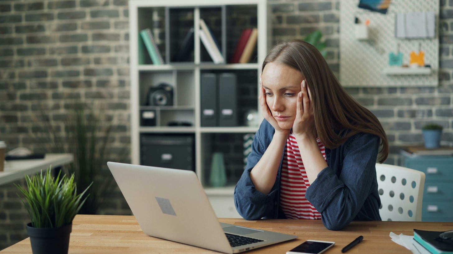 A white woman cups her hands around her chin and stares at her laptop in a stressed manner. A white woman cups her hands around her chin and stares at her laptop in a stressed manner.