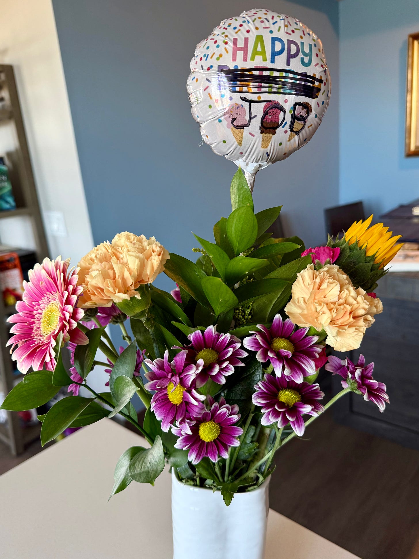Flowers from Tom with a "Happy Birthday" balloon except "birthday" is scribbled out and replaced with "job" to read "Happy JOB"