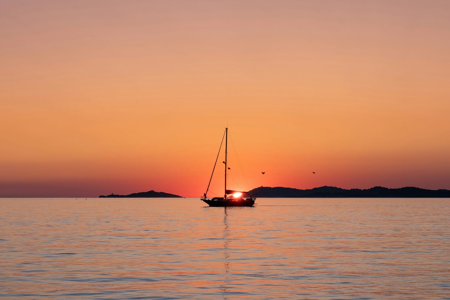 A boat on calm waters. The sun is low in the sky and the scene has a warm orange glow.