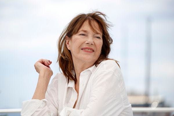 Imagem: Jane Birkin sentada olhando para o lado, usando camisa branca numa foto mais recente.