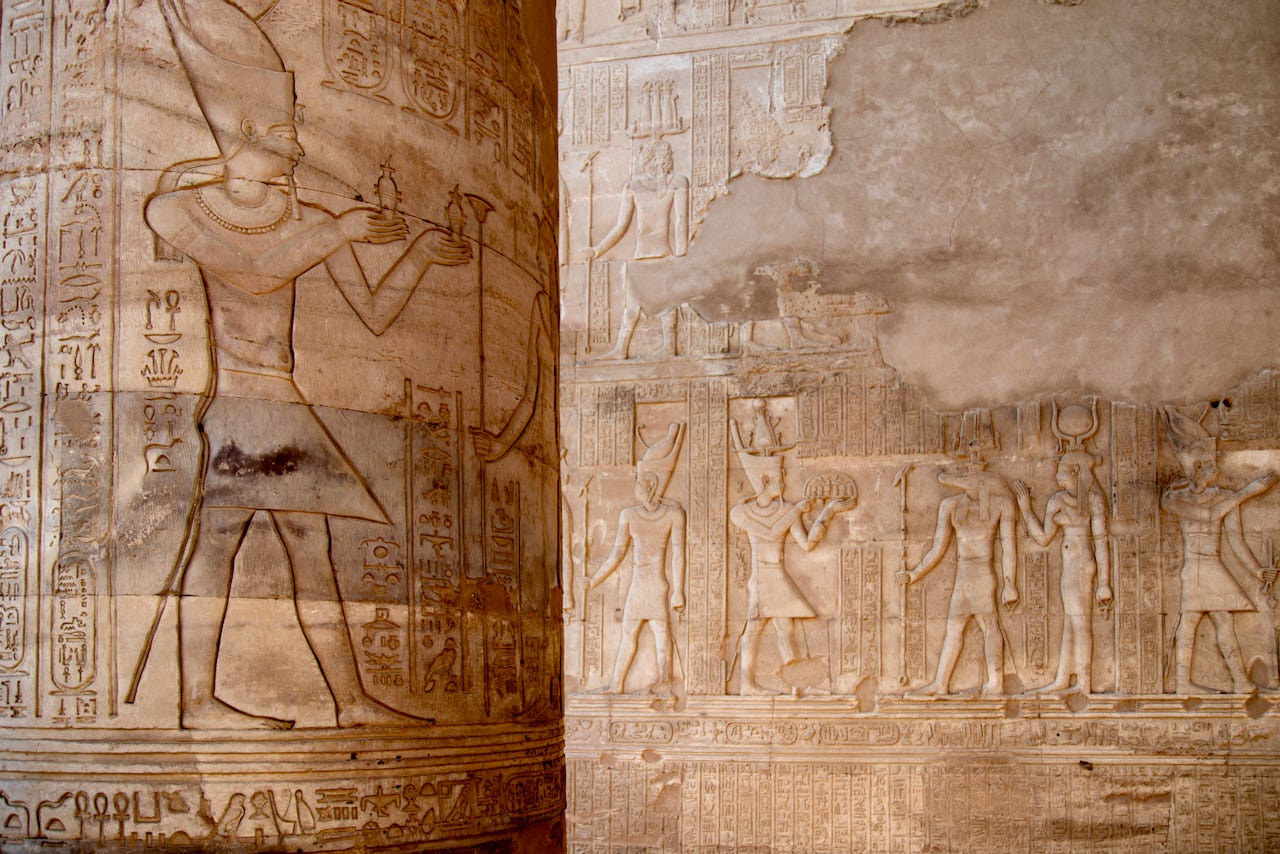 Carved reliefs on a column and wall inside the Temple of Kom Ombo, showing Egyptian deities and hieroglyphic inscriptions in warm sandstone