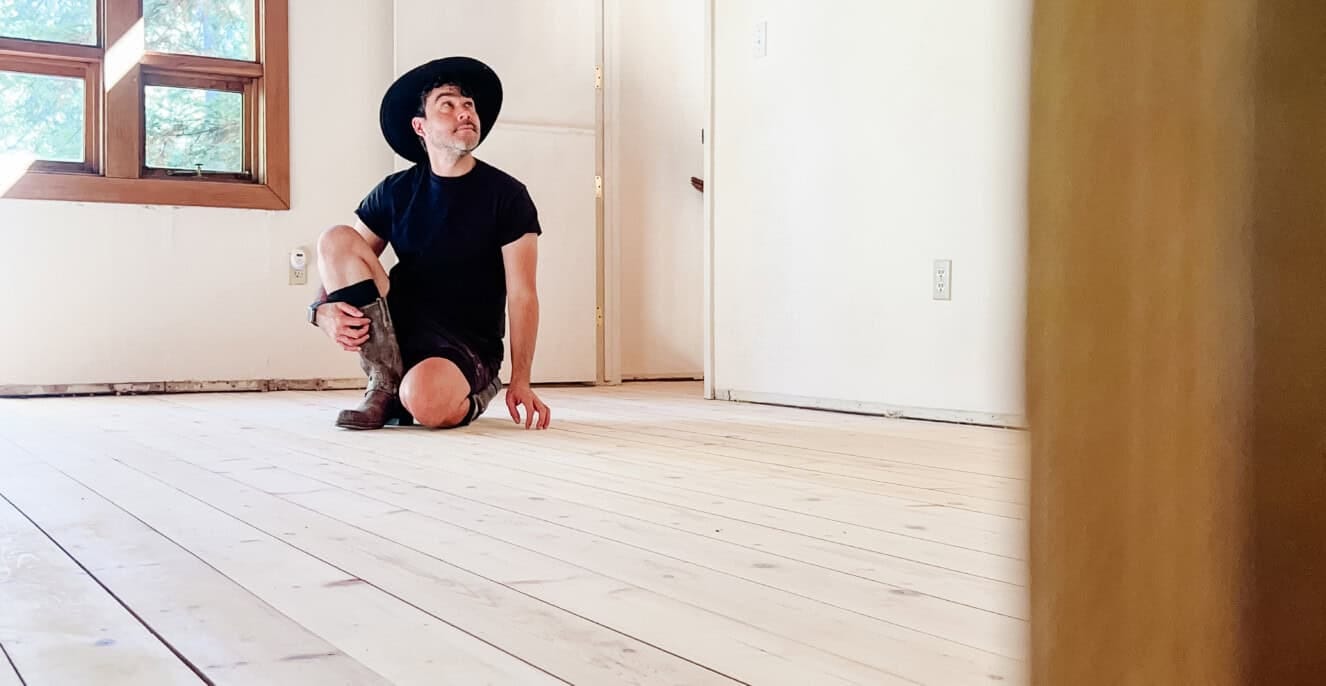 hardwood pine floors restoration, freshly sanded in an empty room with anthony sitting on it with a giant window. behind him.