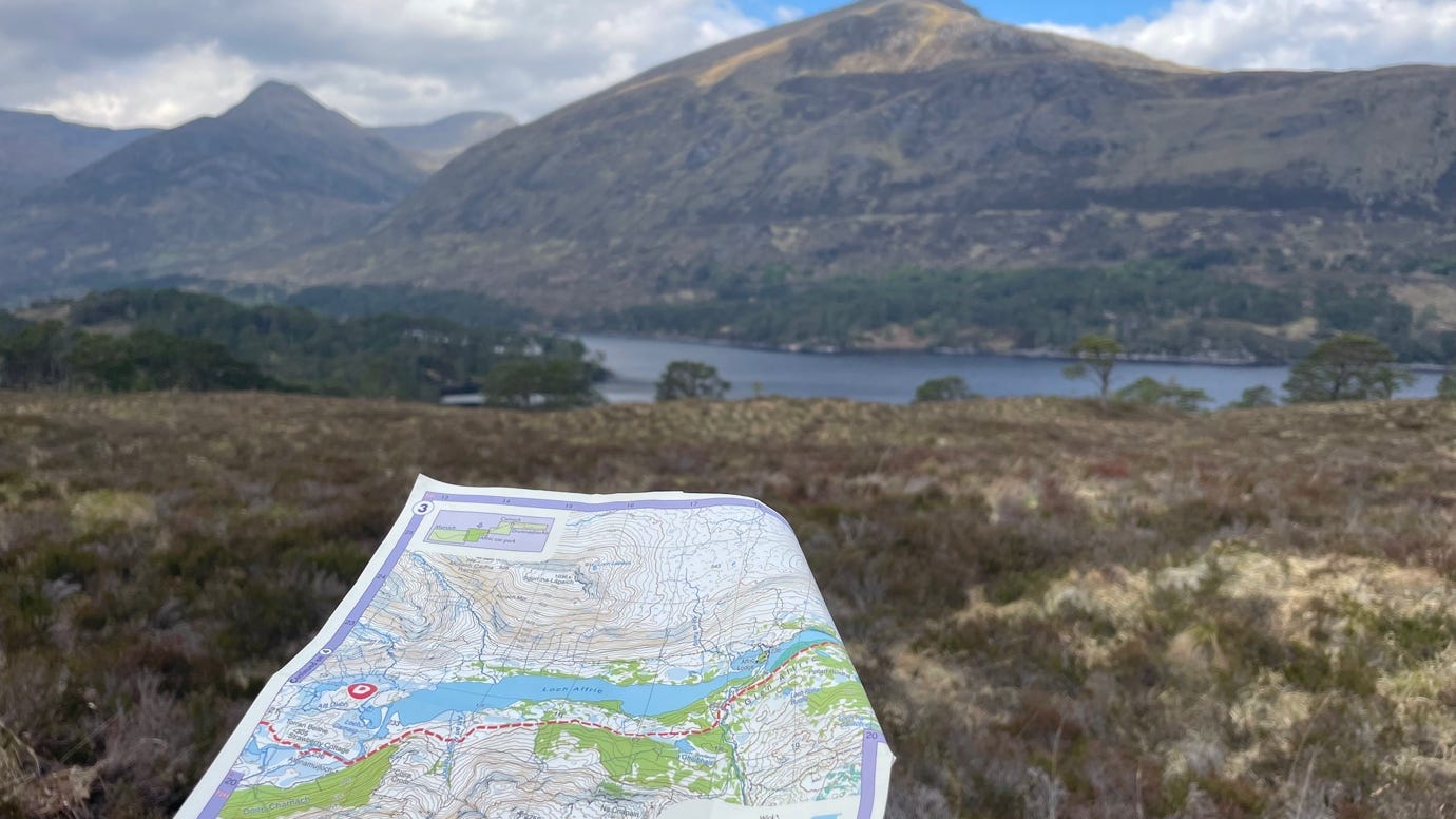 A hand holding a map in front of a mountain

AI-generated content may be incorrect.